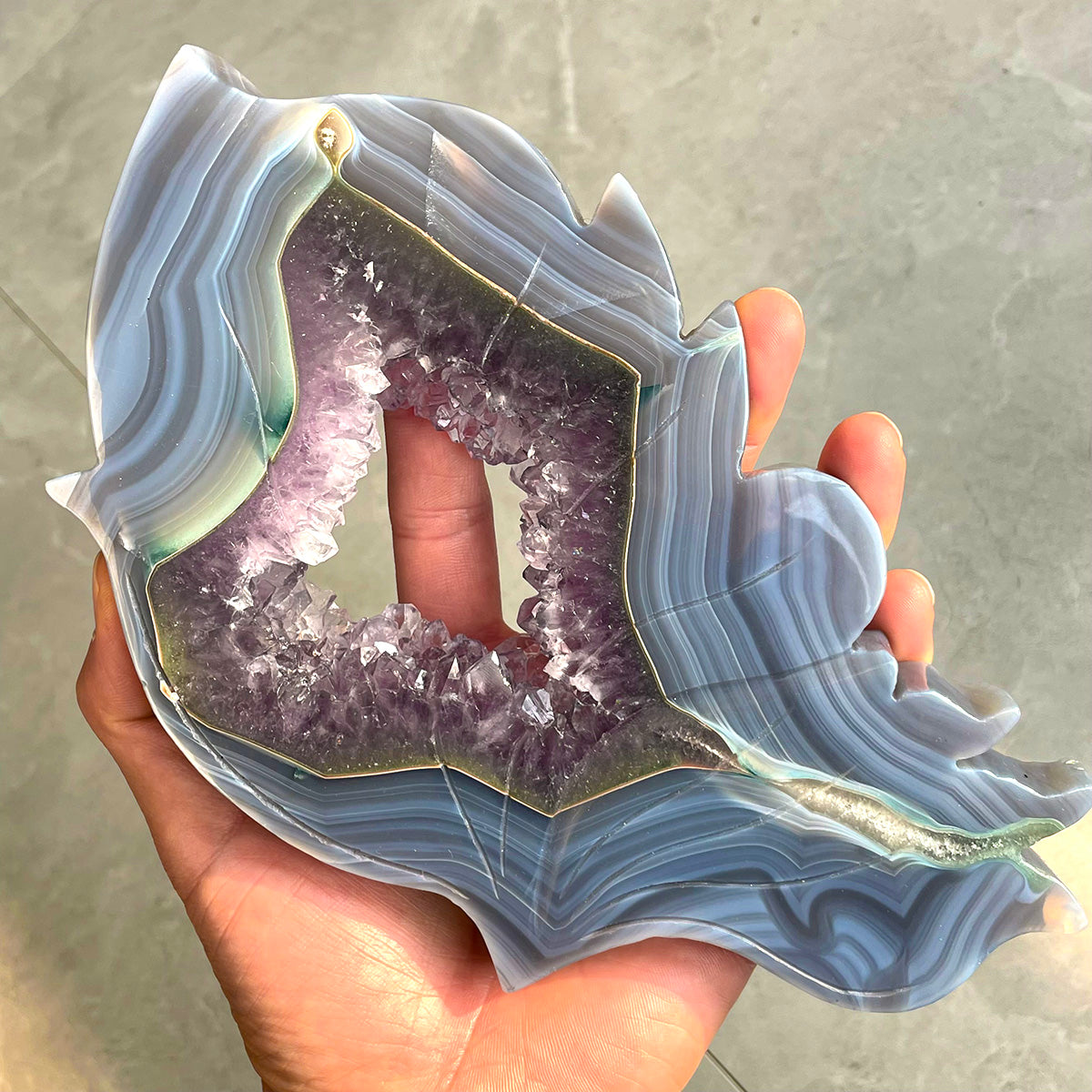 A hand holding a large agate and amethyst butterfly wing to show its scale and detail.