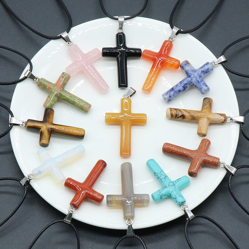 A collection of thirteen assorted crystal and gemstone cross pendants on a white plate