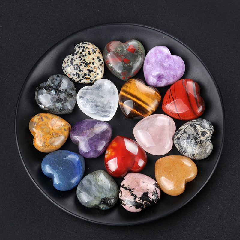 A collection of assorted polished crystal hearts on a black plate, including Dalmatian Jasper and Tiger's Eye
