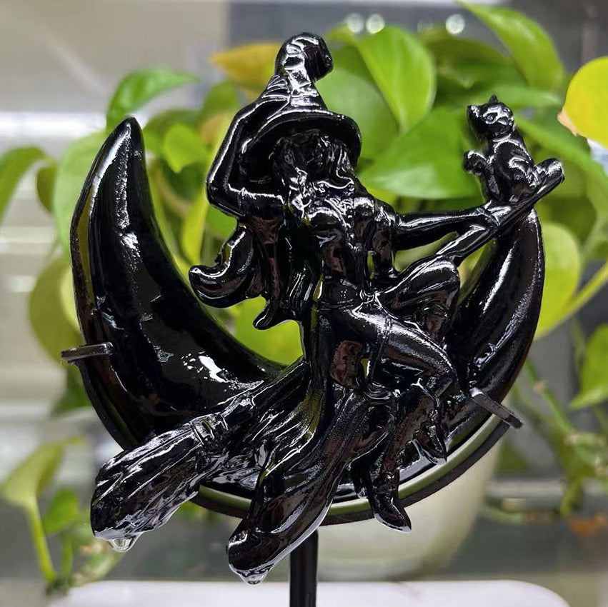 Polished Black Obsidian carving of a witch and cat on a crescent moon, displayed on a stand