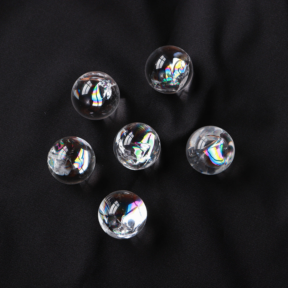A collection of six mini clear quartz crystal balls with rainbow inclusions on a black surface.