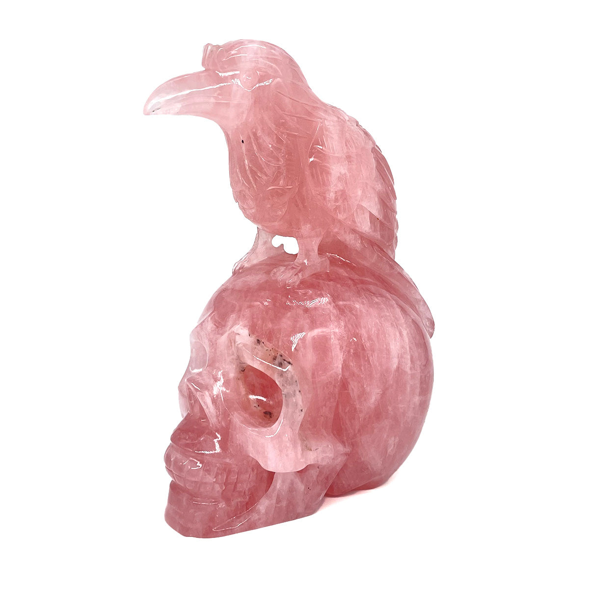 Angled view of a hand-carved rose quartz skull with raven, showing detail in the eye socket.
