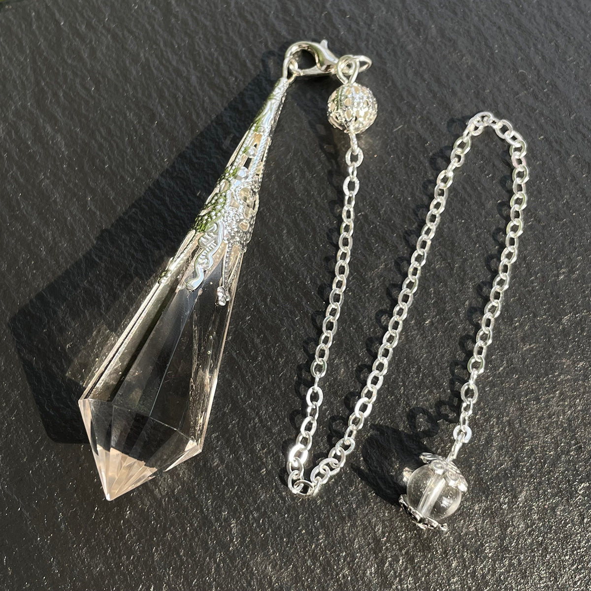 Full view of the clear quartz pendulum showing the faceted point, cap, and chain with a quartz bead.