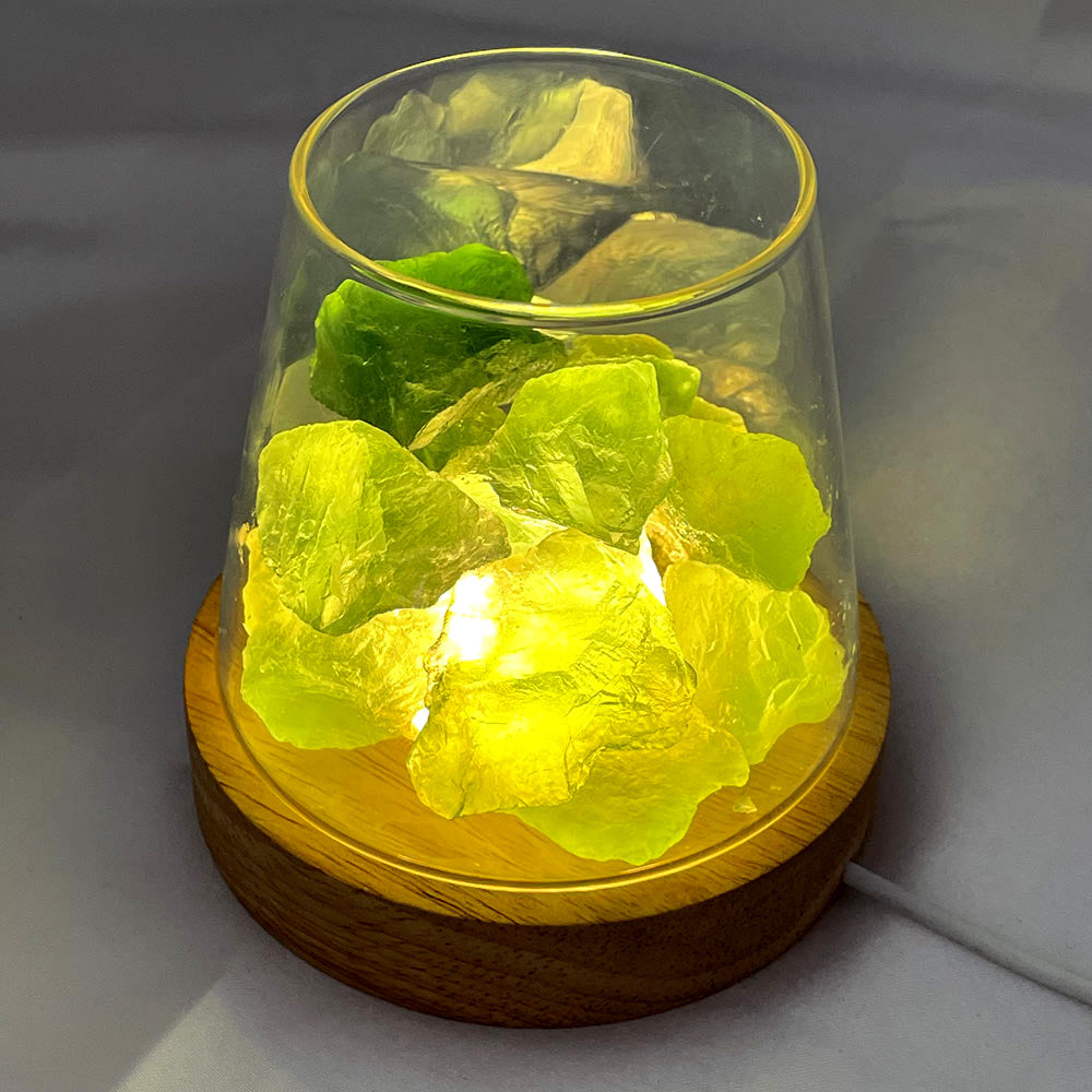 A crystal lamp with raw green fluorite glowing brightly with a warm yellow light from its wooden LED base