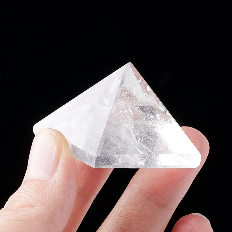 Fingers holding a small 3cm clear quartz pyramid to show its size and clarity