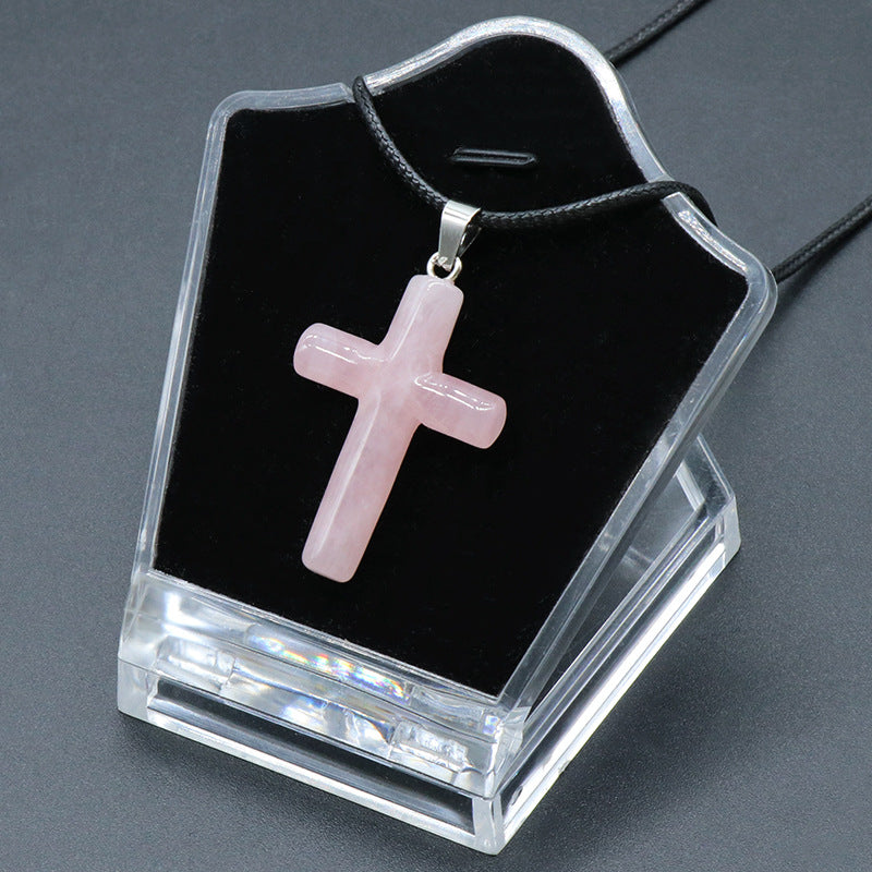 A polished rose quartz cross pendant necklace on a black display stand