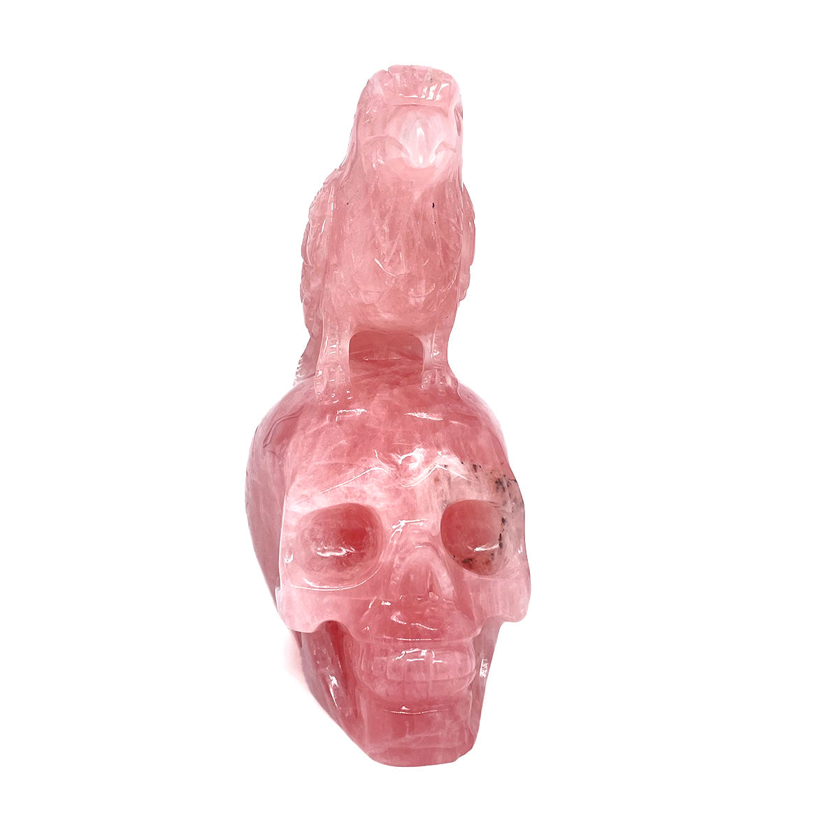 Front view of a pink rose quartz skull and raven sculpture against a white background.