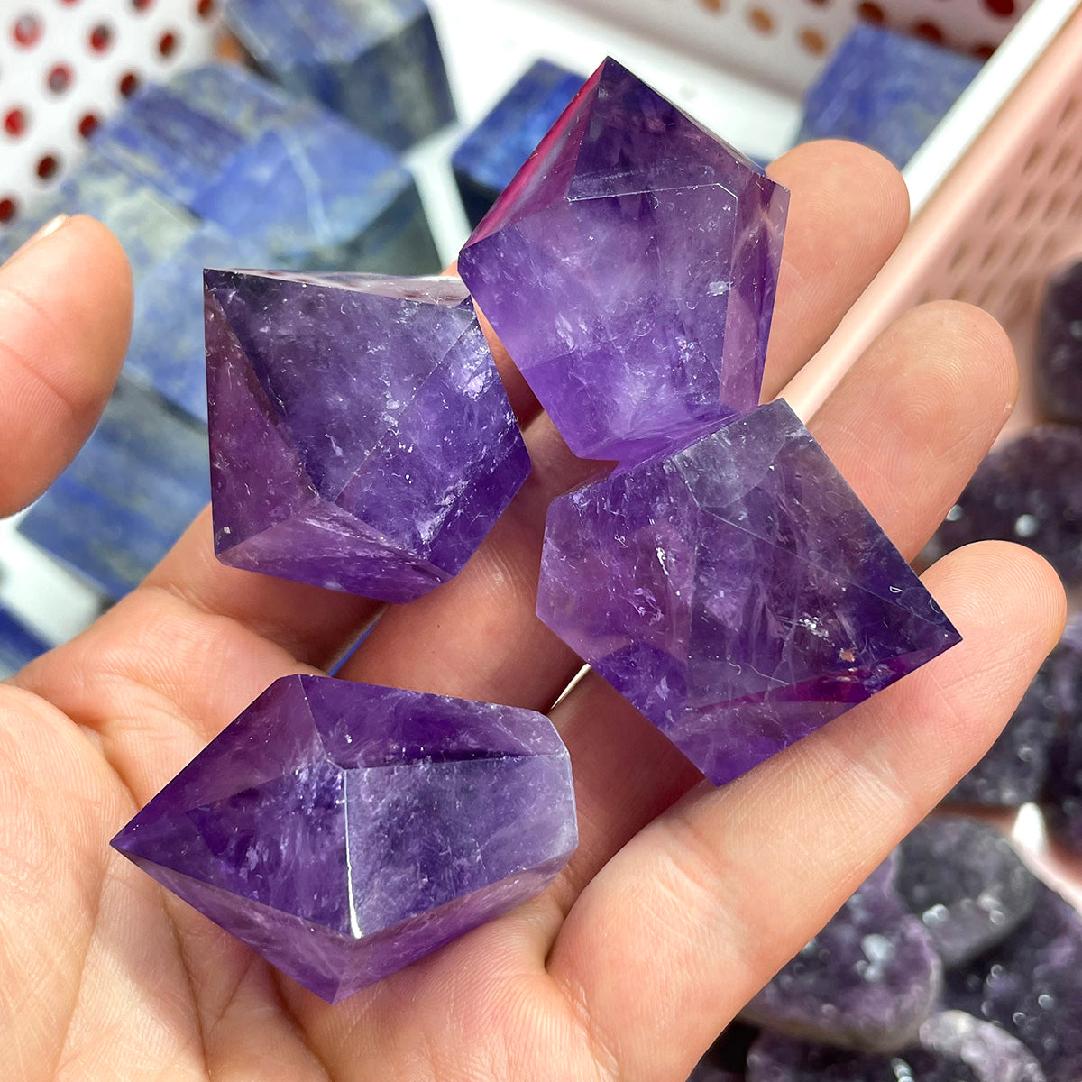 A hand holding four small natural amethyst points to show their quality