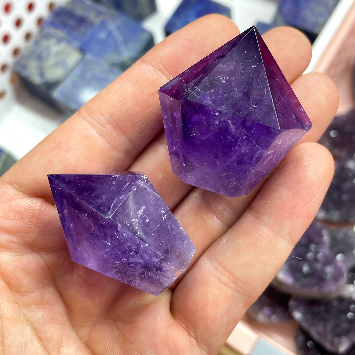 Two mini amethyst crystal points of different sizes held in a palm for comparison