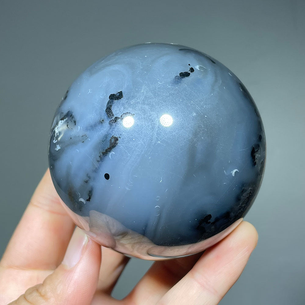 Polished volcanic agate sphere showing its blue-gray color and black dendritic inclusions