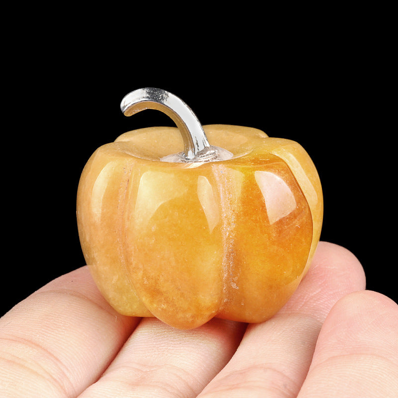 Closeup of a hand-carved yellow jade crystal pumpkin with a silver stem held in hand