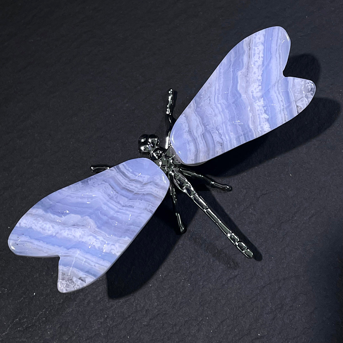 Top-down view of a dragonfly figurine with blue lace agate wings on a dark surface.