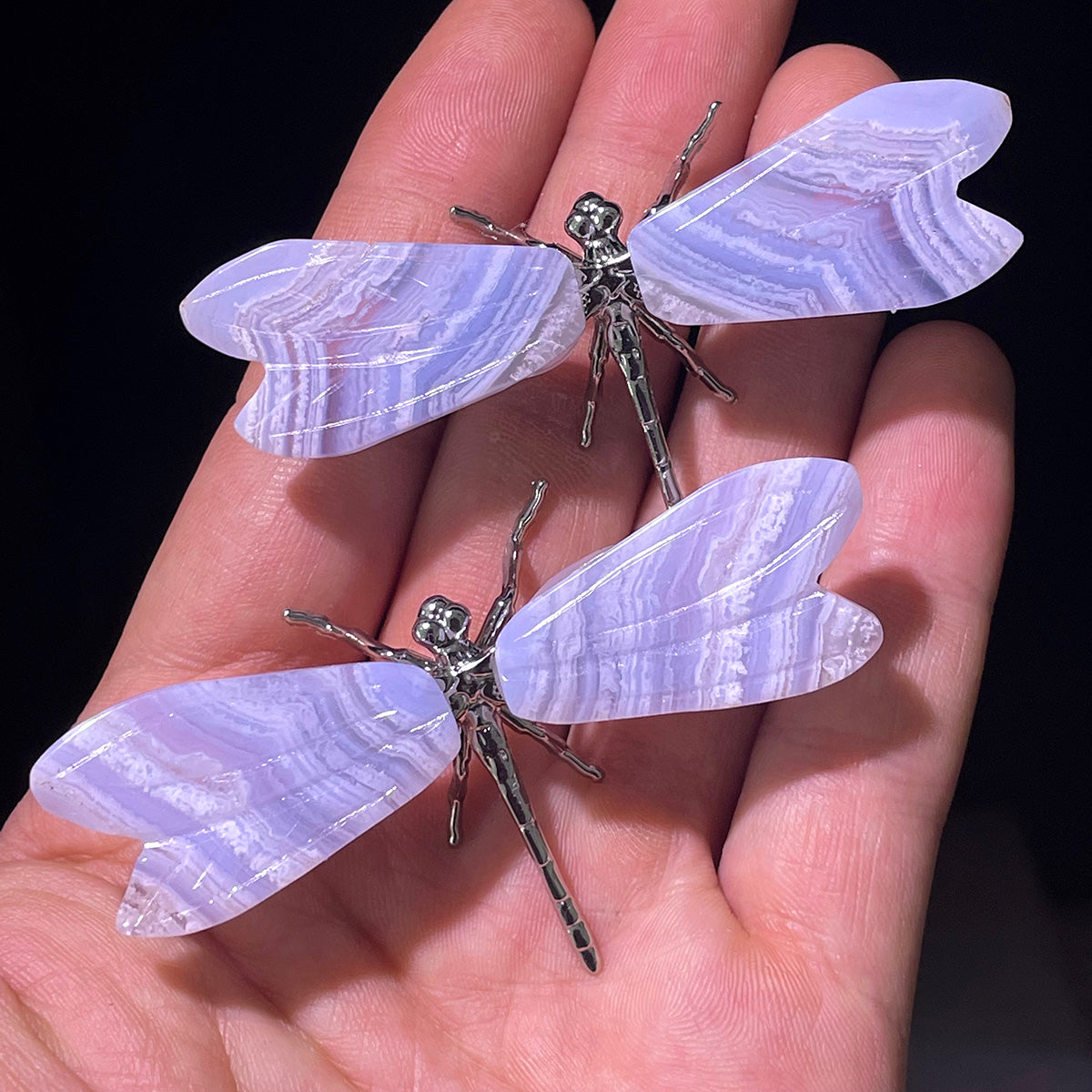 A hand holding two blue lace agate dragonfly figurines to show their size and detail.