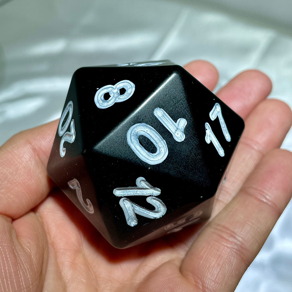 Close up of polished black gemstone D20 dice showing engraved numbers 8, 10, and 17