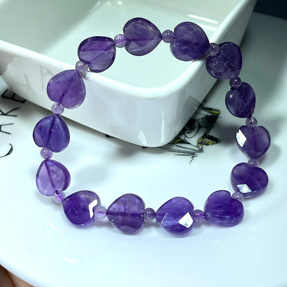 A stretchy bracelet made of deep purple amethyst faceted heart beads on a white dish