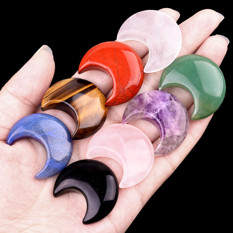 Hand holding a variety of polished crystal crescent moons, including amethyst, rose quartz, and tiger's eye.