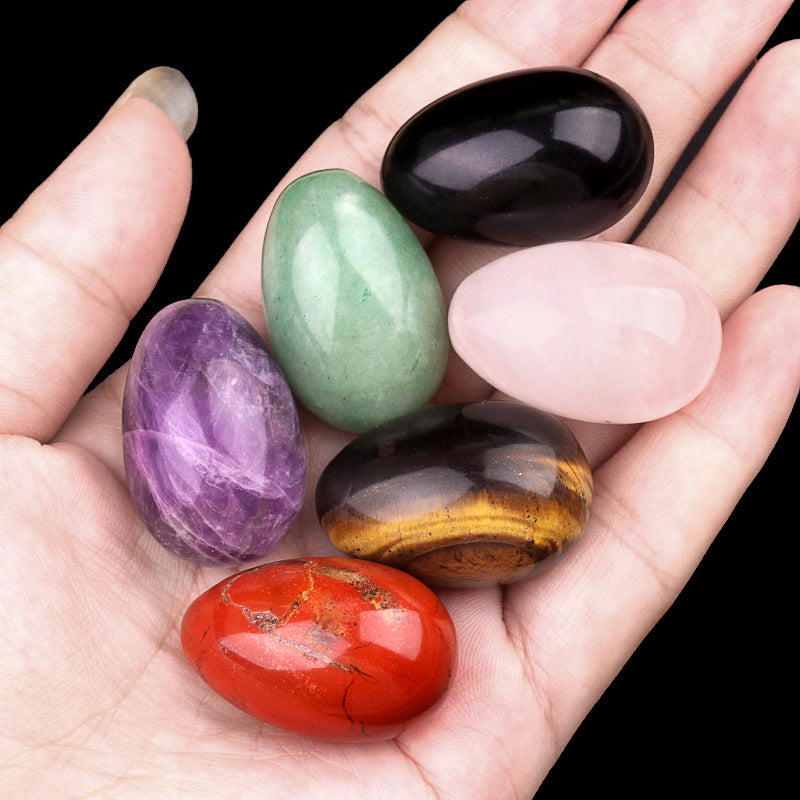 Hand holding 6 assorted polished crystal eggs, including amethyst, rose quartz, and tiger's eye.