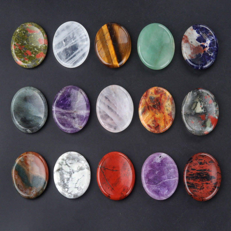 A collection of fifteen assorted oval-shaped crystal worry stones on a black background