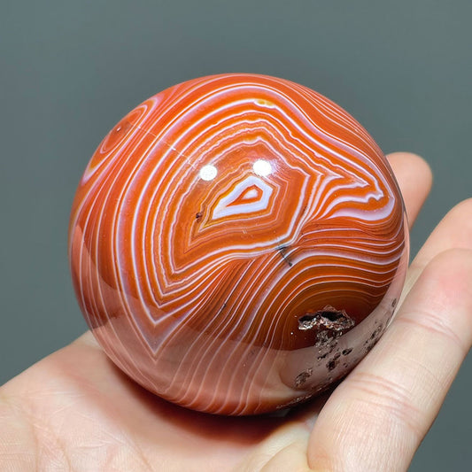 Hand holding a polished carnelian agate sphere with a prominent eye pattern.