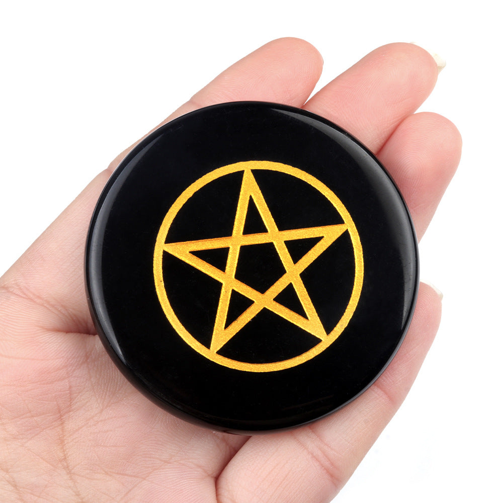 Black circular object with a yellow pentagram held in a hand against a white background