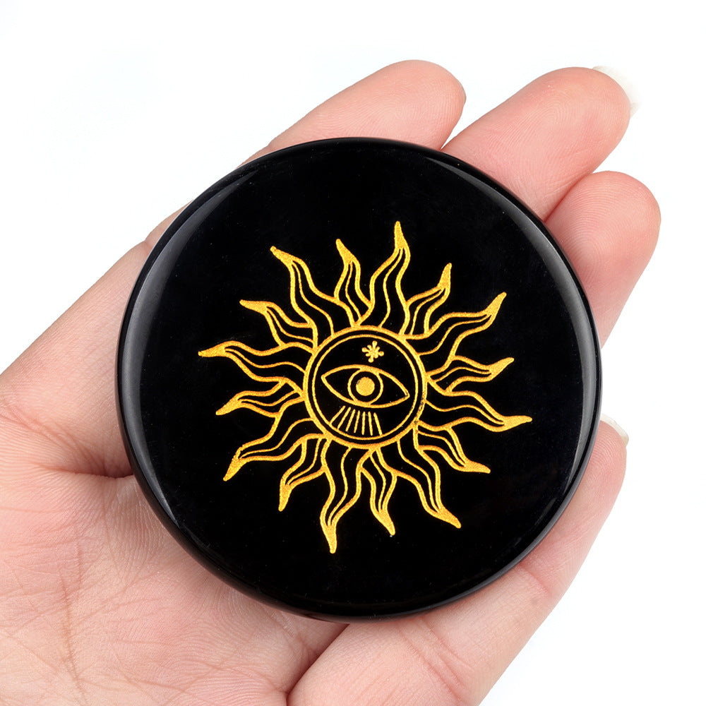 Black circular object with yellow sun and eye design held in a hand against a white background