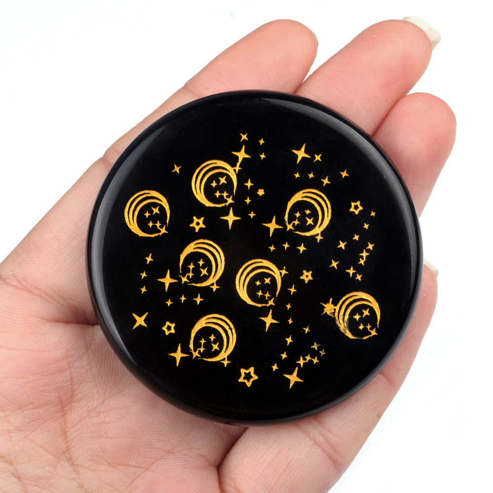 Round black object with yellow star and moon designs held in a hand against a white background
