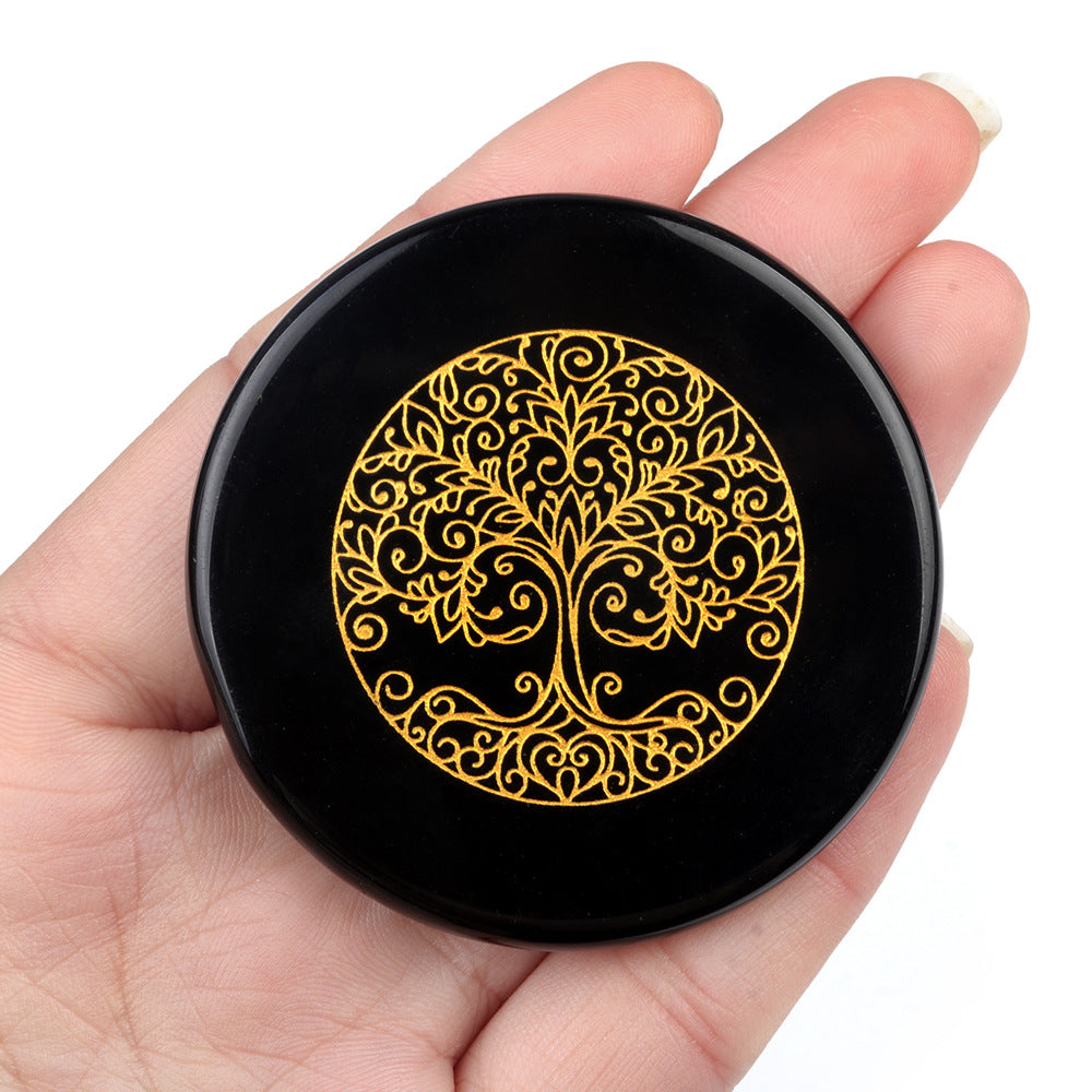 Black circular object with gold tree of life design held in a hand against a white background