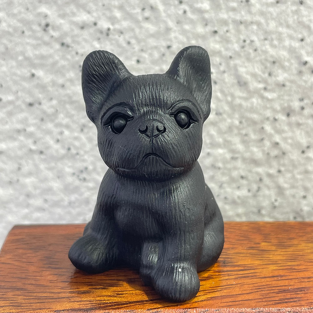 A detailed closeup of a hand-carved black obsidian French Bulldog figurine