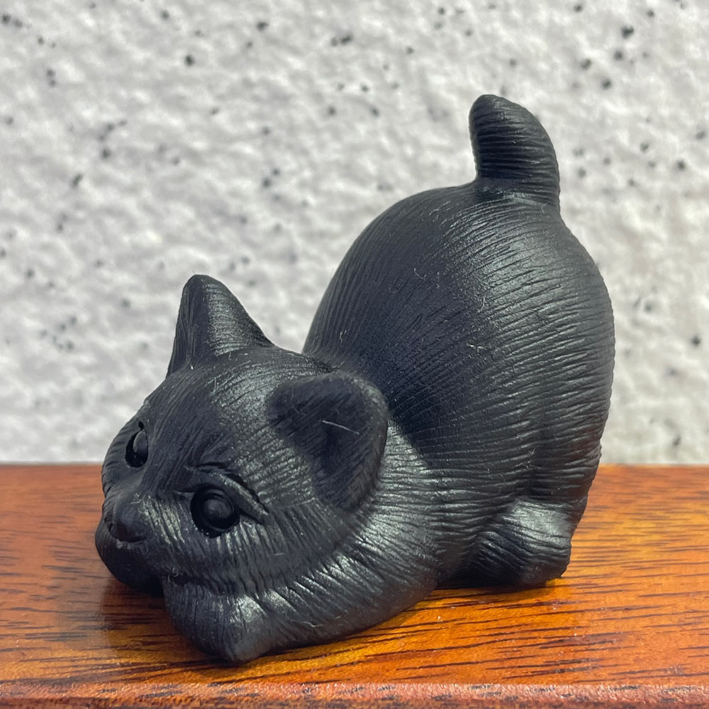 A hand-carved black obsidian cat in a playful pounce pose with its tail up