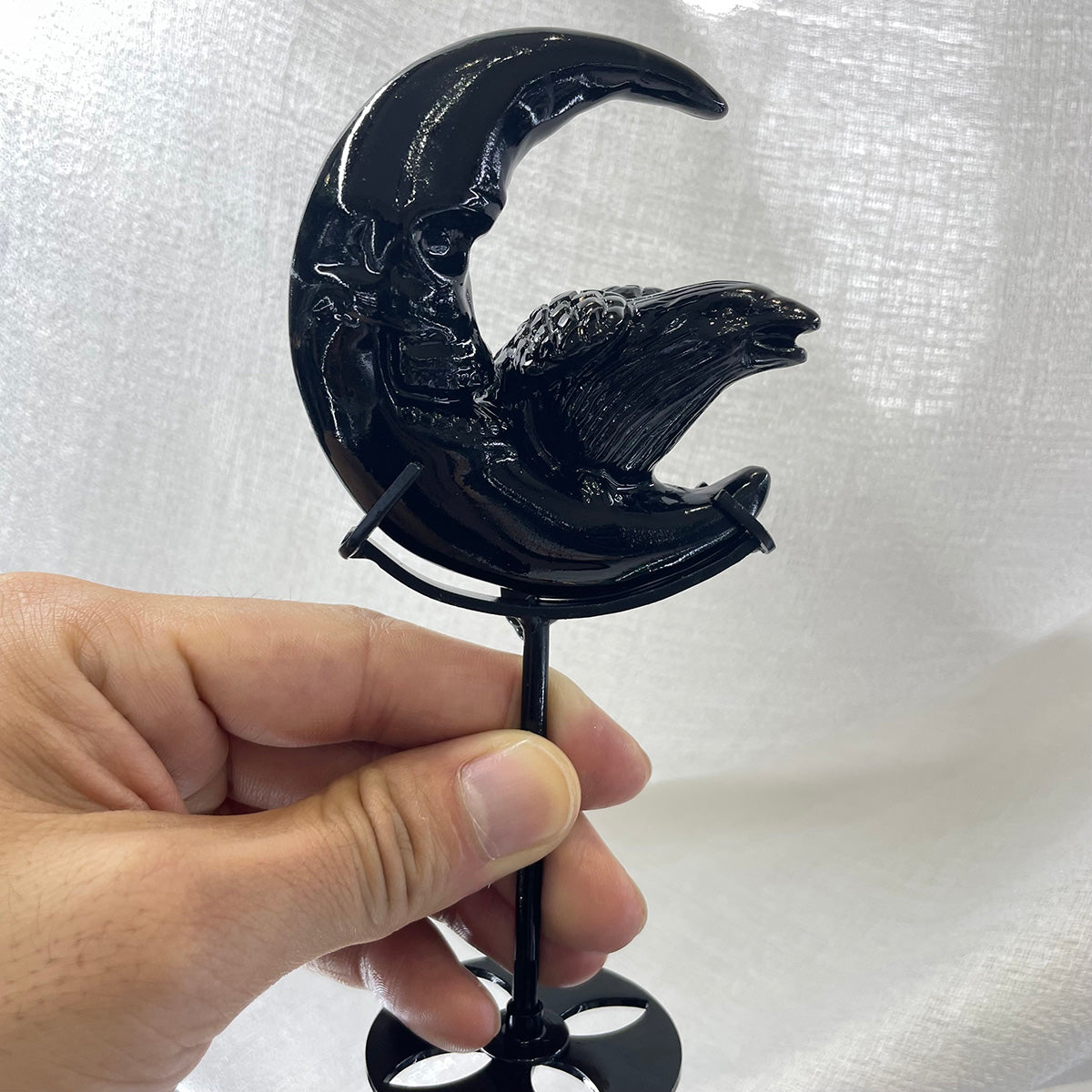 Full view of the black obsidian raven and skull moon carving on its metal display stand.