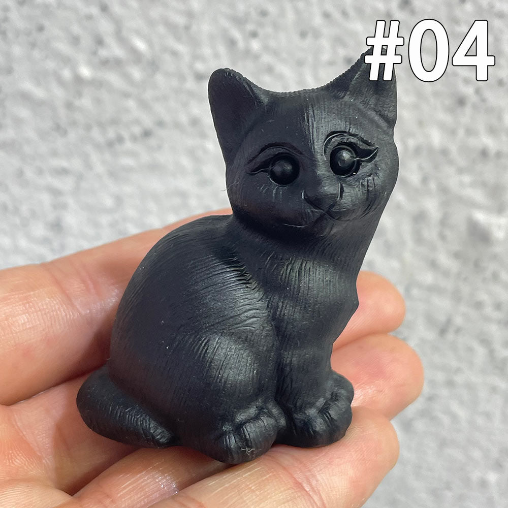 A hand holding a small, detailed black obsidian figurine of a sitting cat