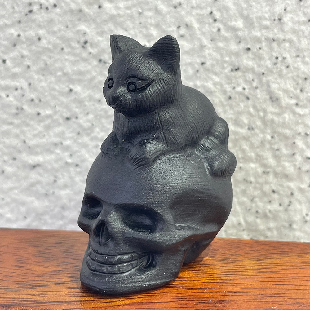 A black obsidian crystal skull with a small cat familiar sitting on top