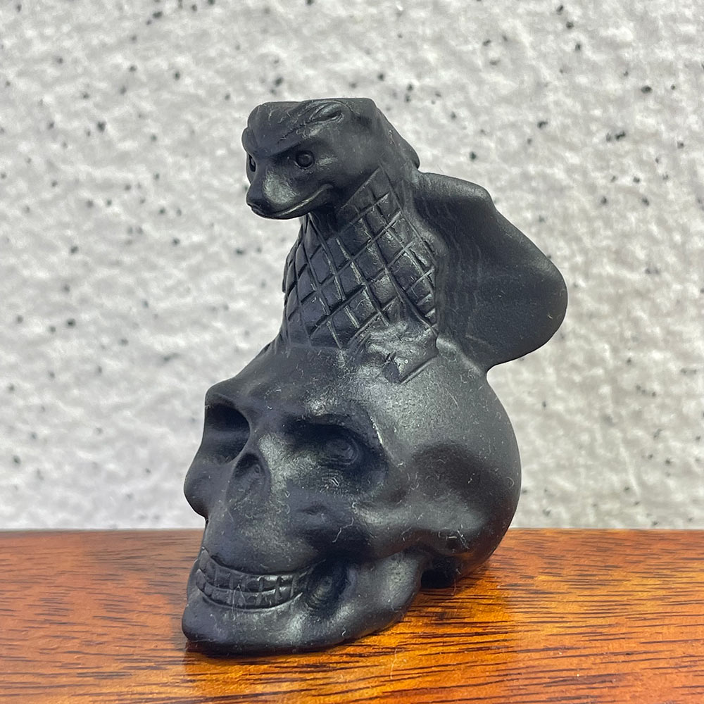 A black obsidian skull featuring a carved dragon with scaled details on top