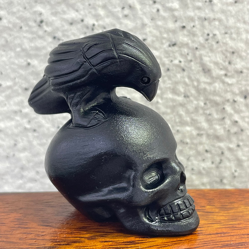 Side profile of a black obsidian skull with a detailed raven carving perched on top