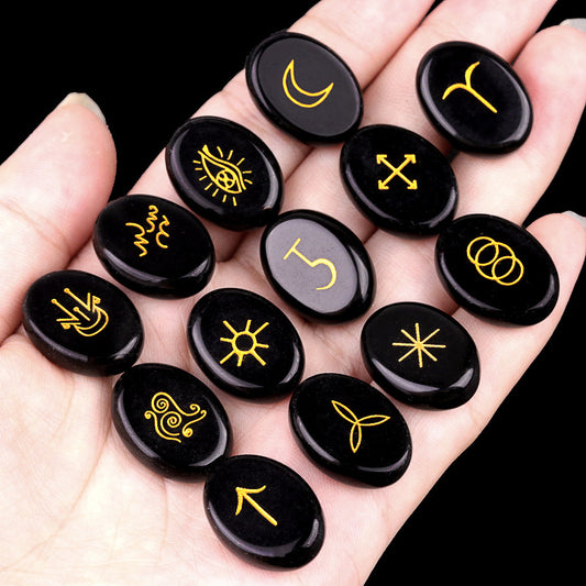 Hand holding a set of 13 black obsidian stones engraved with gold modern Witch's Rune symbols