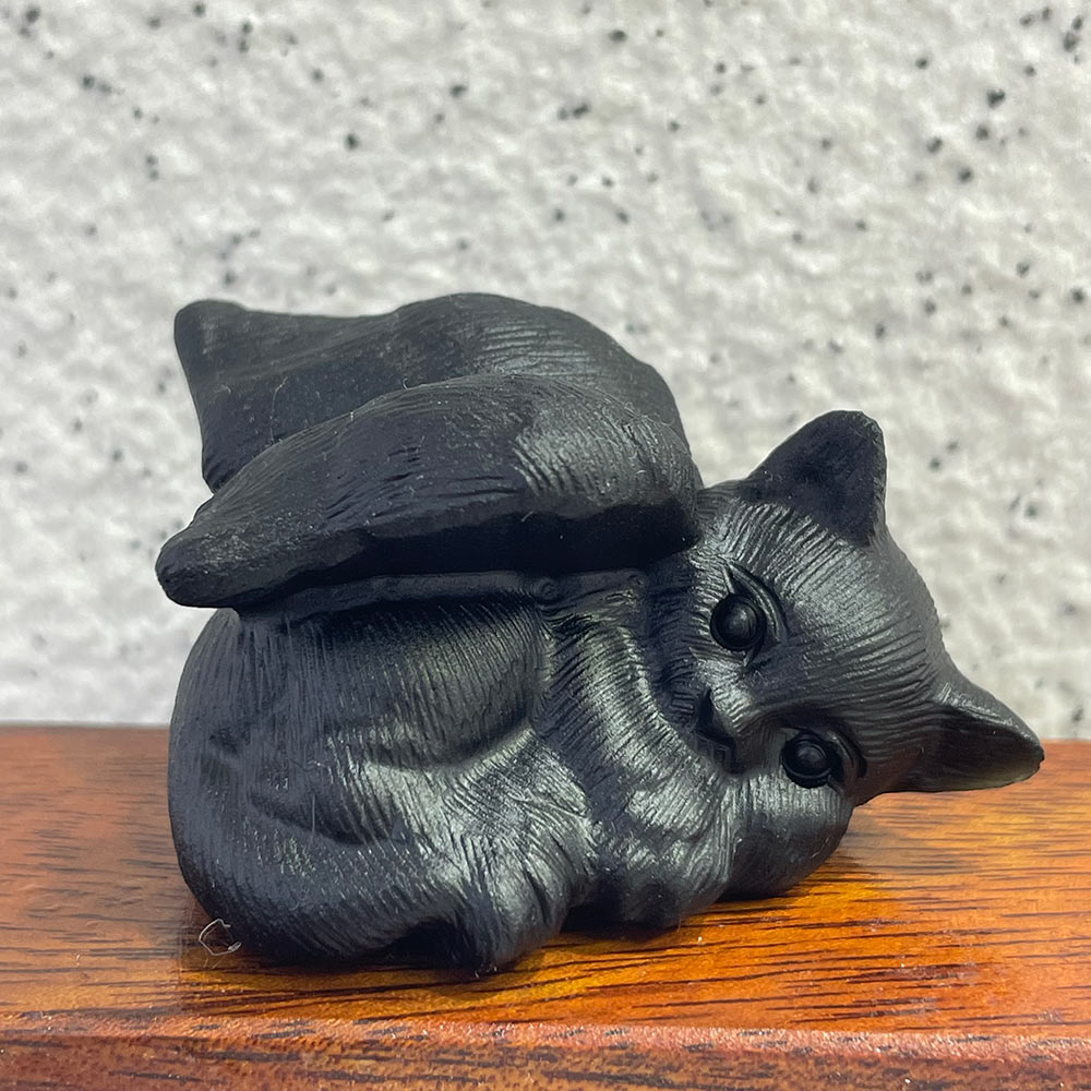 Black obsidian cat figurine on a wooden surface with a textured gray background
