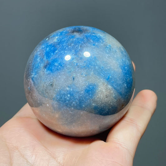 Hand holding a polished blue and grey Trolleite crystal sphere.