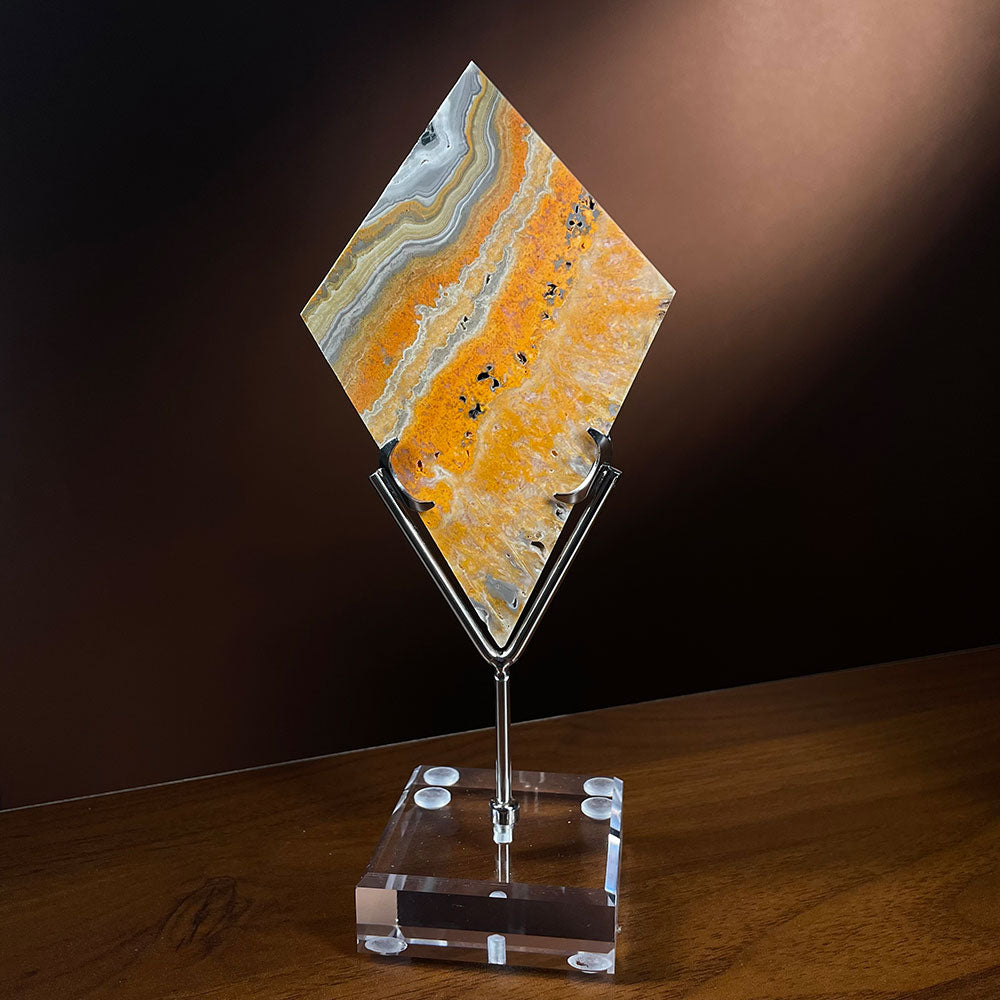 A high quality vibrant yellow and black bumblebee jasper crystal cut into a diamond shape, resting on a clear acrylic and metal display stand.