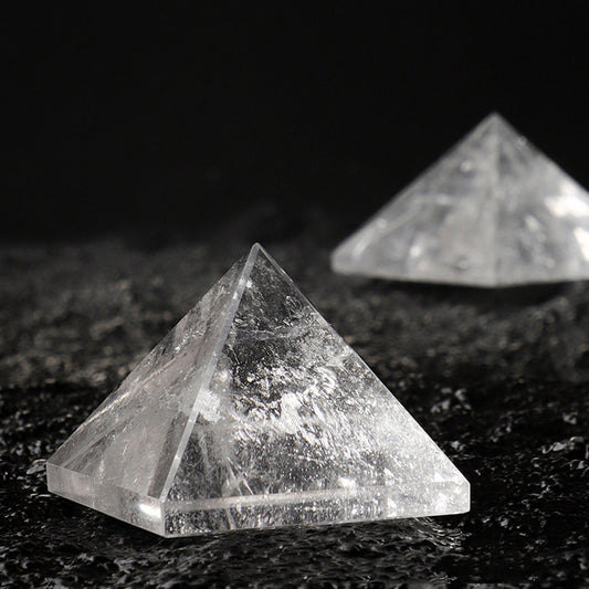A close-up of a polished clear quartz pyramid showing its internal inclusions on a dark surface