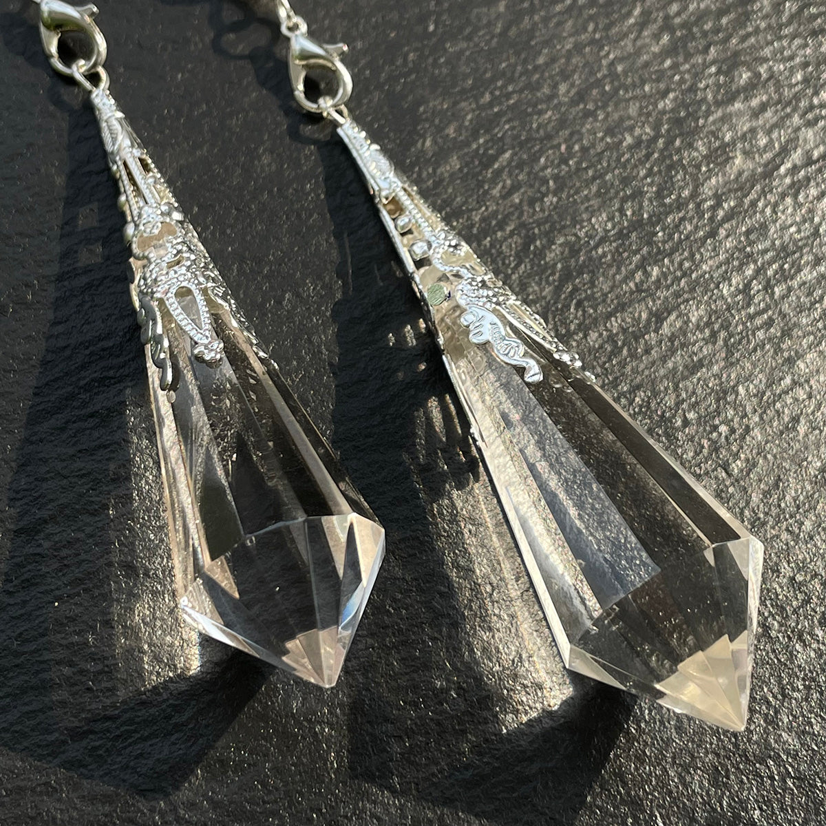 A pair of clear quartz divination pendulums with ornate caps, shown side-by-side.
