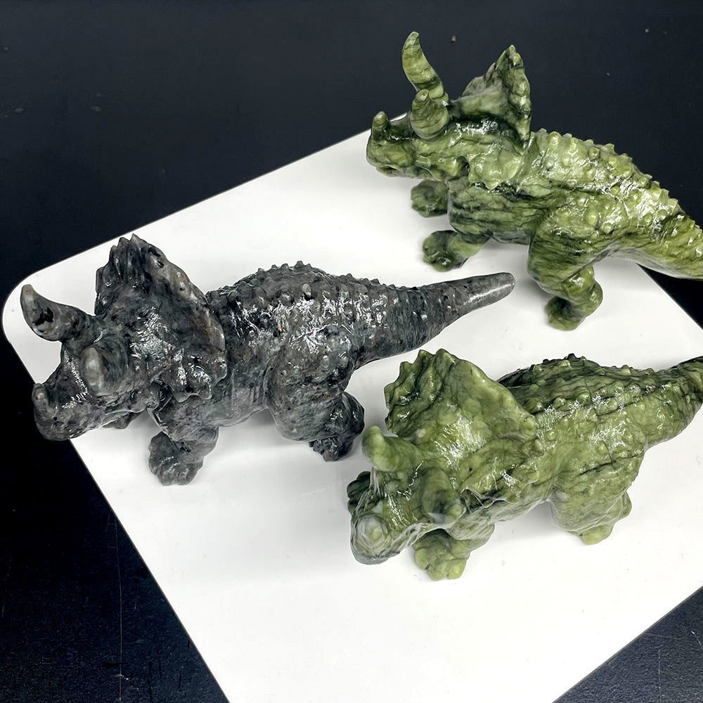 Three triceratops dinosaur figurines in different colors on a white surface with a black background.