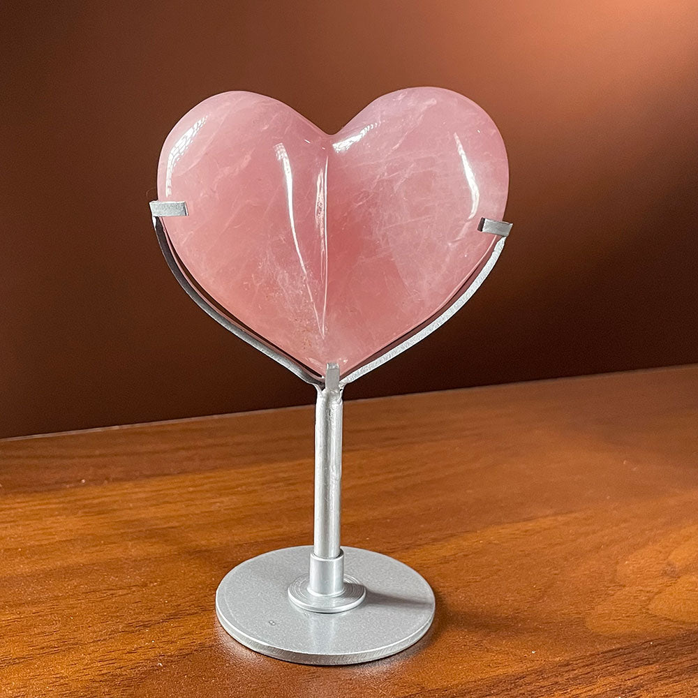 A highly polished, saturated deep pink natural rose quartz bubble heart resting on a modern silver metal display stand