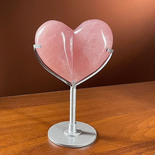 A highly polished, saturated deep pink natural rose quartz bubble heart resting on a modern silver metal display stand