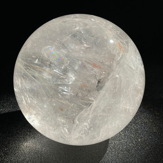 A massive 2.49kg highly transparent natural clear quartz crystal sphere displaying brilliant internal rainbow flashes against a dark background.