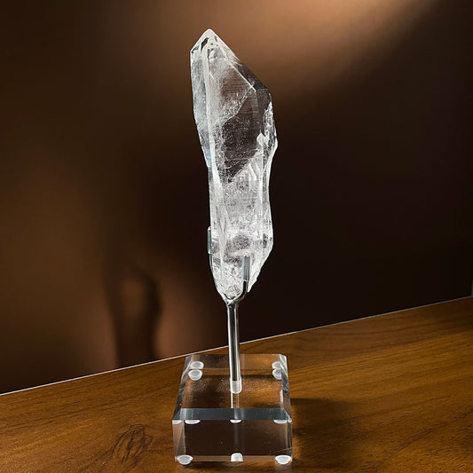 A water-clear, flawless natural Himalayan quartz crystal point resting vertically on a clear acrylic display stand.
