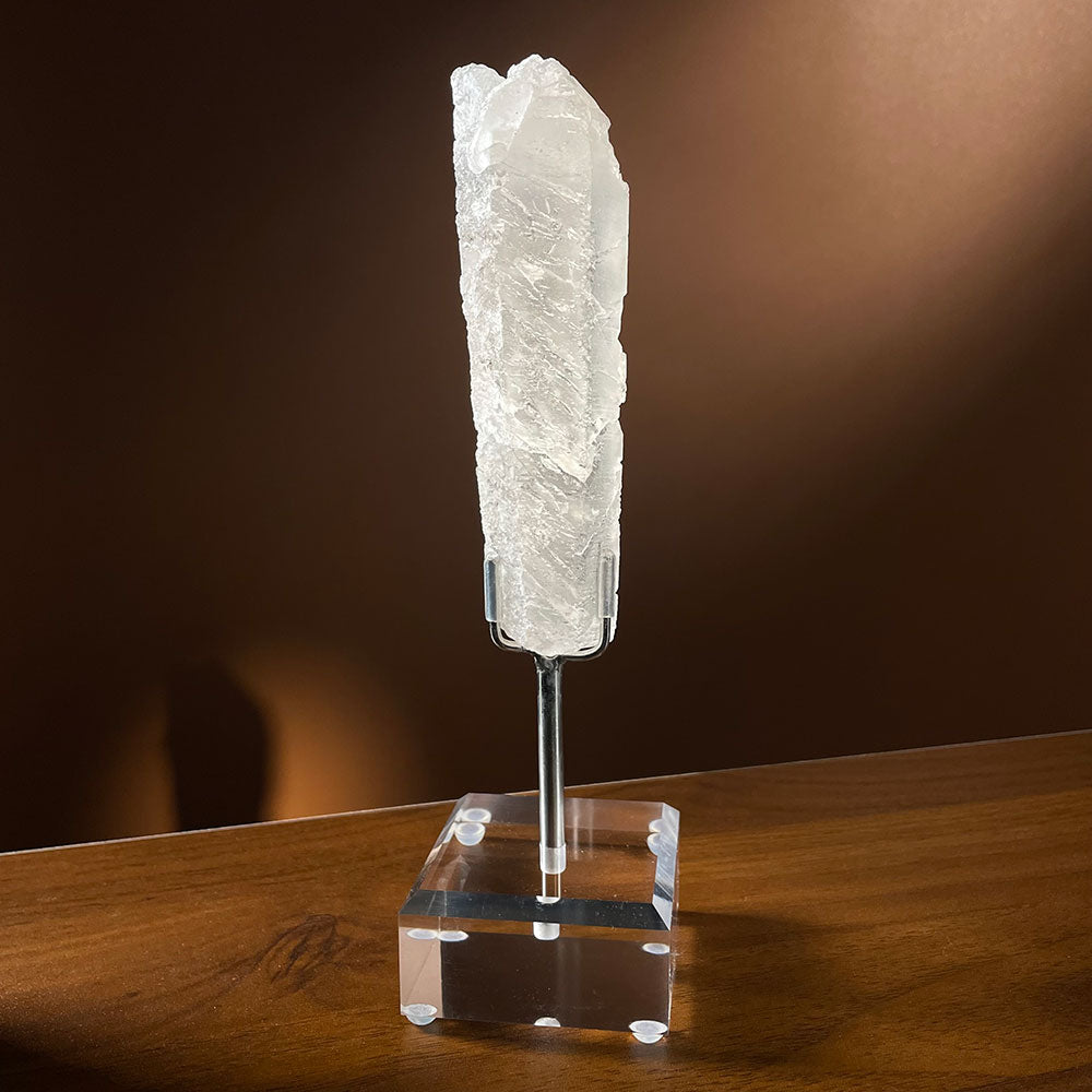  A raw natural growth interference quartz crystal from Madagascar featuring deep horizontal cuts, resting on an acrylic display stand.