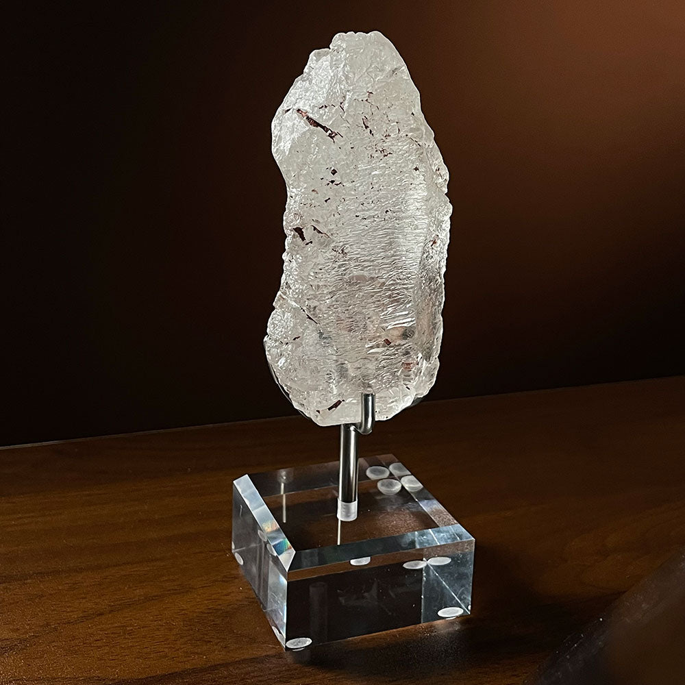 A raw, deeply etched natural Nirvana Quartz crystal from Madagascar, resembling melting glacial ice, resting on a clear acrylic display stand.