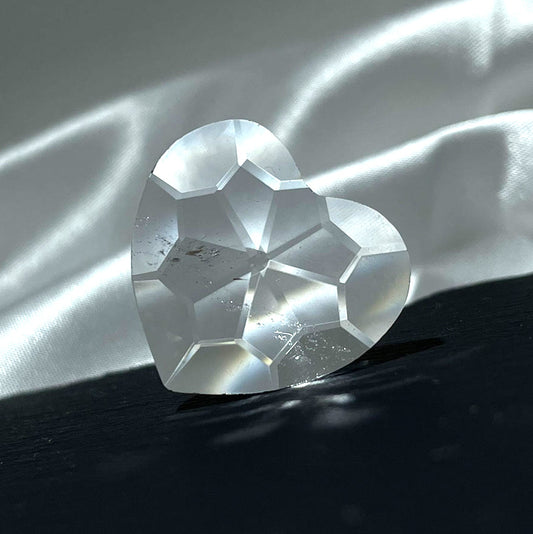 An angled view of a brilliant, gem-cut clear quartz heart showing its intricate facets