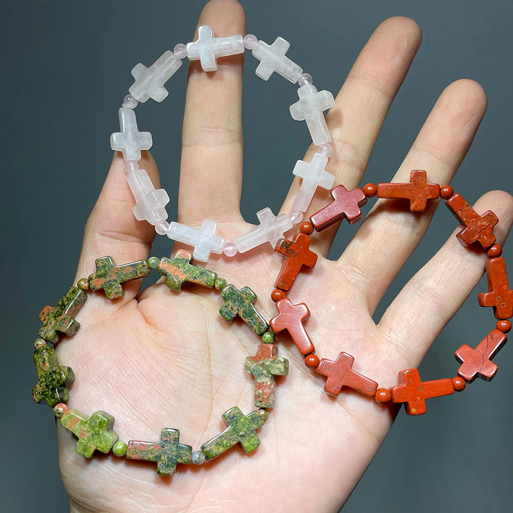 Three gemstone cross bracelets in Rose Quartz, Unakite, and Red Jasper held in a hand.