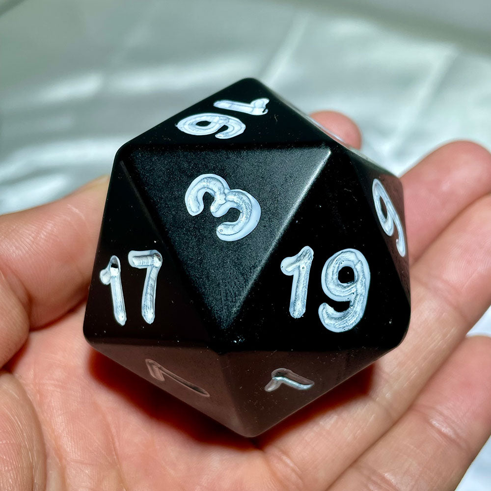Large 60mm natural black obsidian 20-sided die with white numbers being held in a hand to show scale